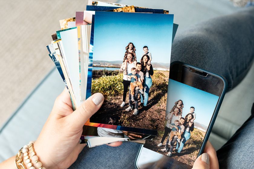Hands holding printed photos and a phone, both showing the same family portrait outdoors