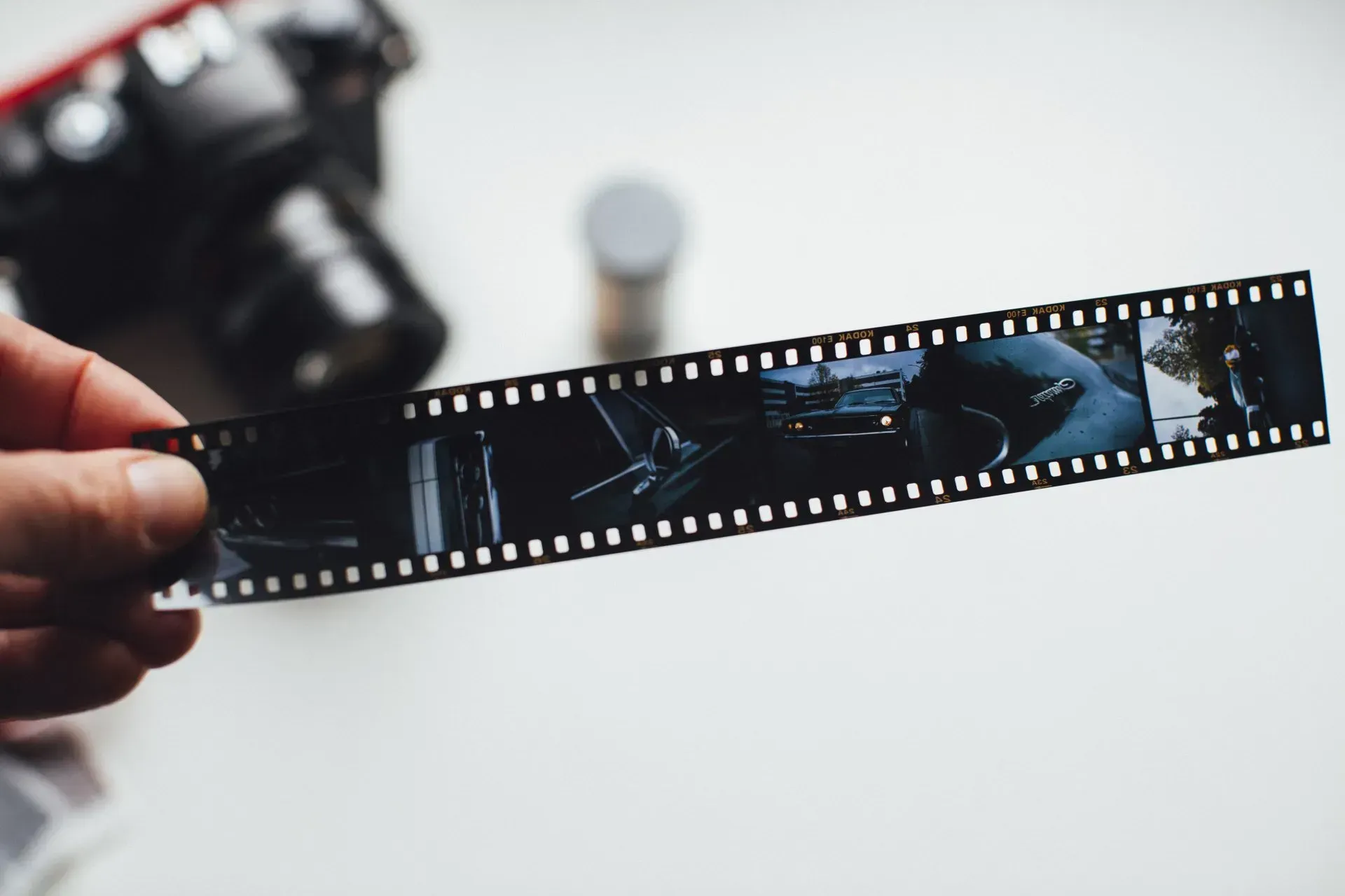 Hand holding a strip of developed film negatives with a blurred camera in the background.