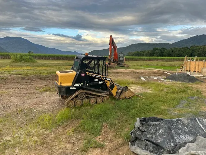Excavator in a field with mountain in the back — Cairns Earthmoving Solutions In Holloways Beach, QLD