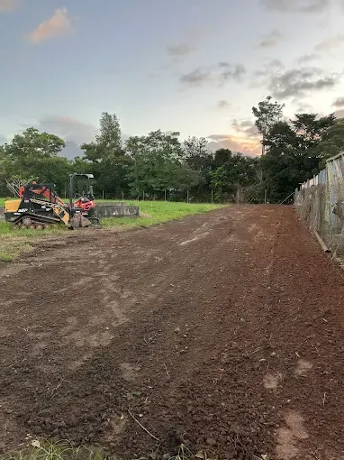 Dirt and gradd field with machine in the back — Cairns Earthmoving Solutions In Gordonvale, QLD