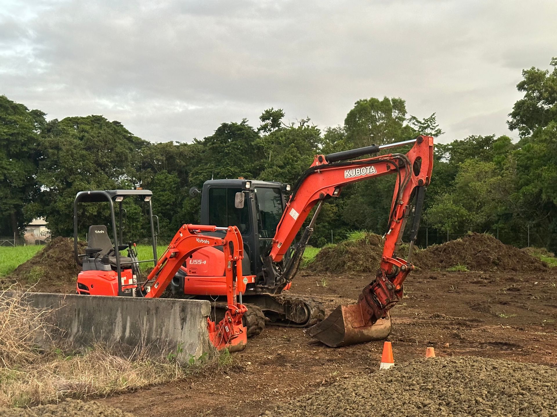 Orange Excavator Digging in a Dirt Field With a Smaller Excavator — Cairns Earthmoving Solutions In Redlynch, QLD