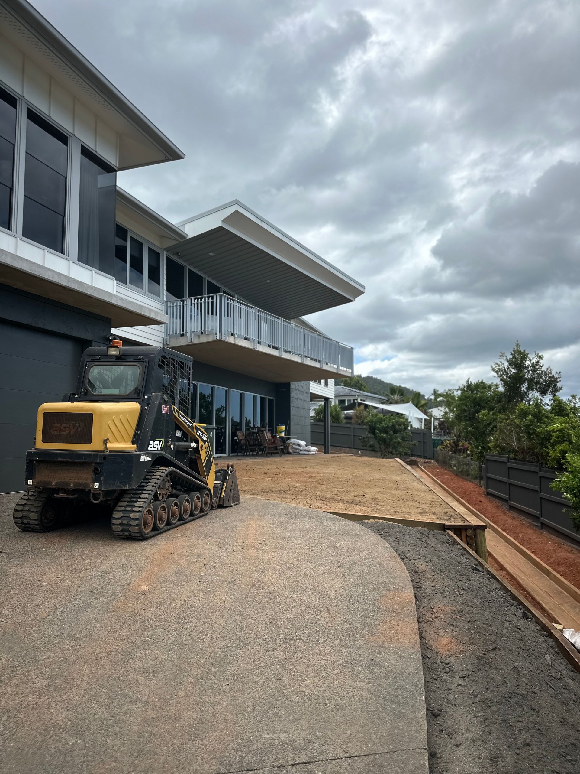 Yellow Construction Vehicle Parked Near a Modern Home — Cairns Earthmoving Solutions In Redlynch, QLD