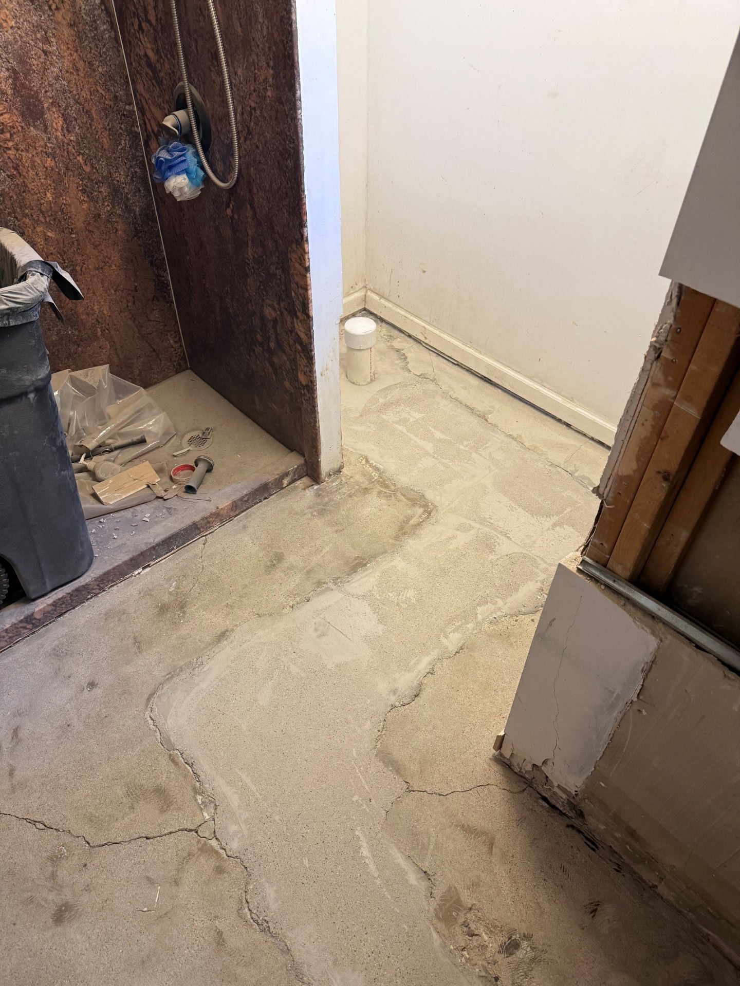 Uneven concrete floor by an open doorway with exposed wall and scattered construction debris.