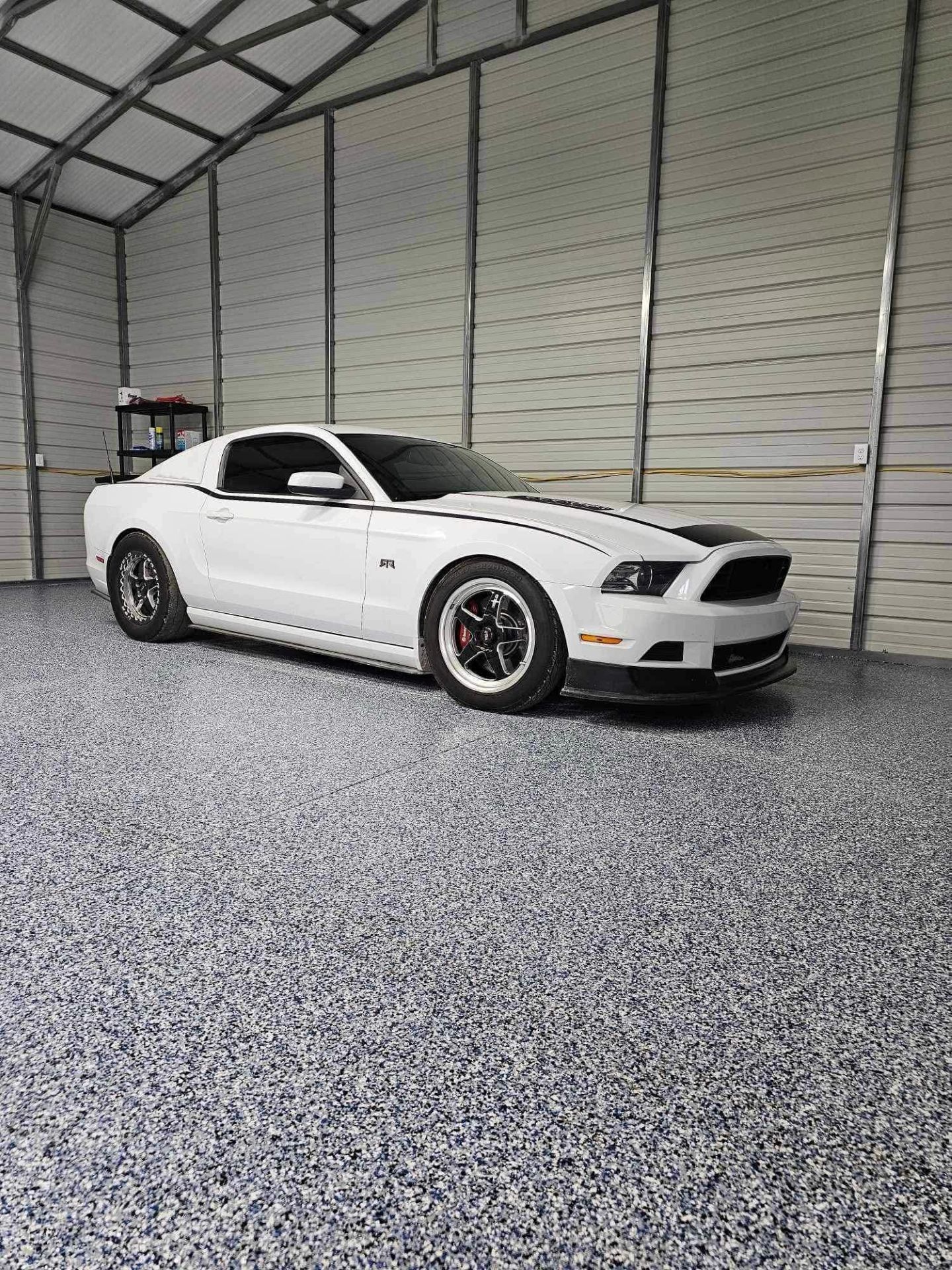 White sports car parked inside a large metal garage on a gravel floor.