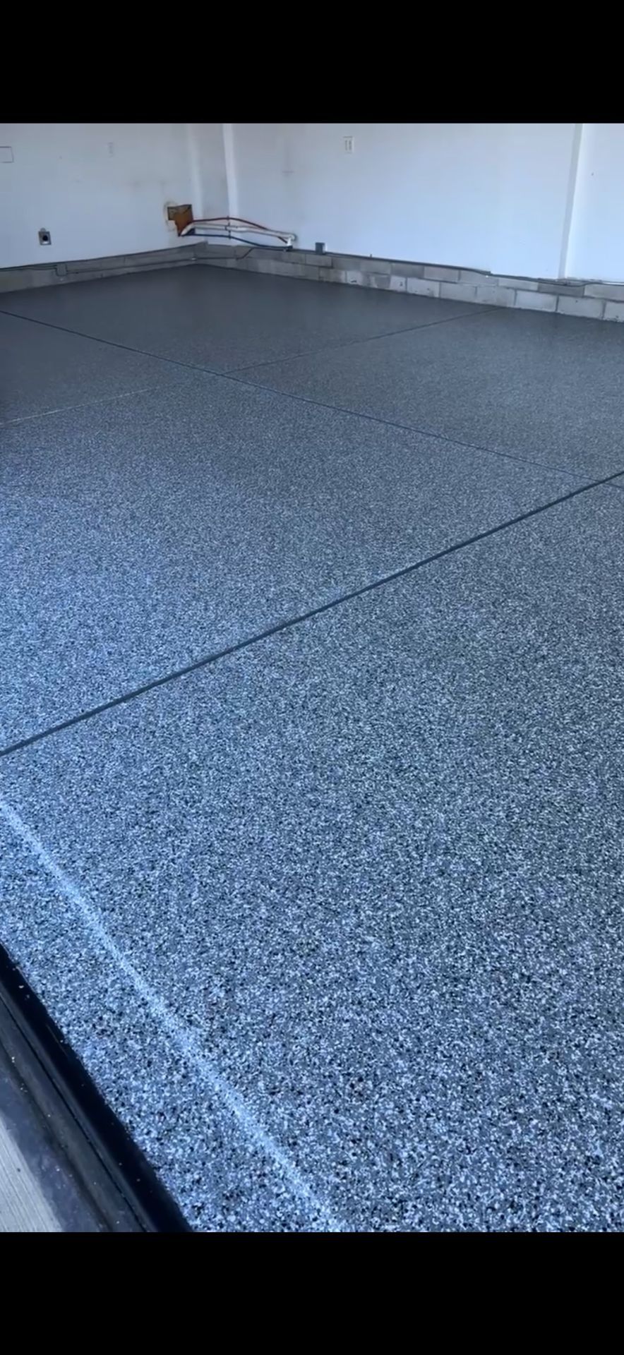 Speckled gray textured floor or rooftop surface beside a white wall and black edge trim