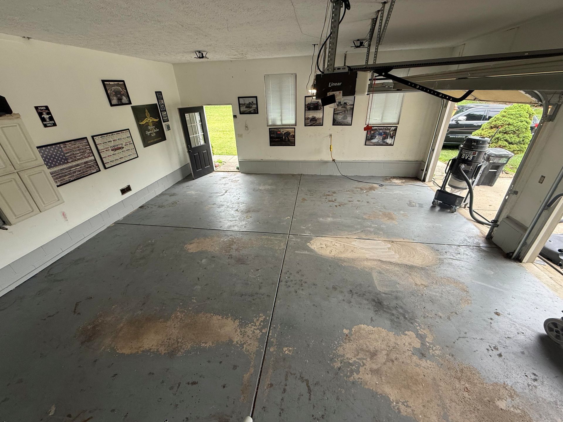 Empty garage interior with concrete floor, wall posters, and an open door to a driveway outside.