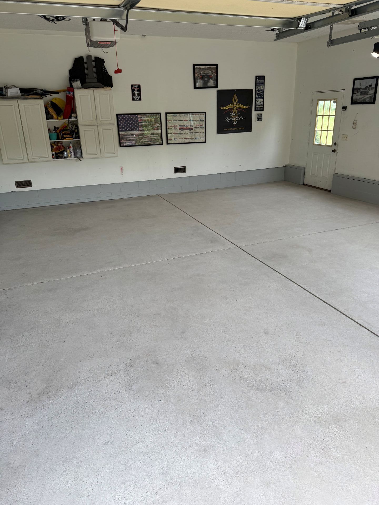 Empty garage interior with white walls, concrete floor, and overhead storage shelves