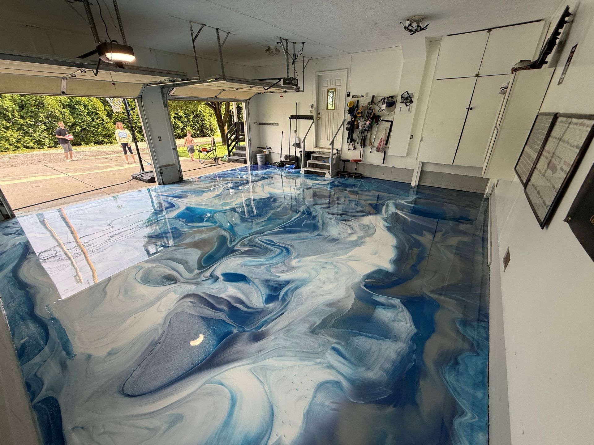 Blue-and-white epoxy floor in an unfinished garage with gym equipment and open side views