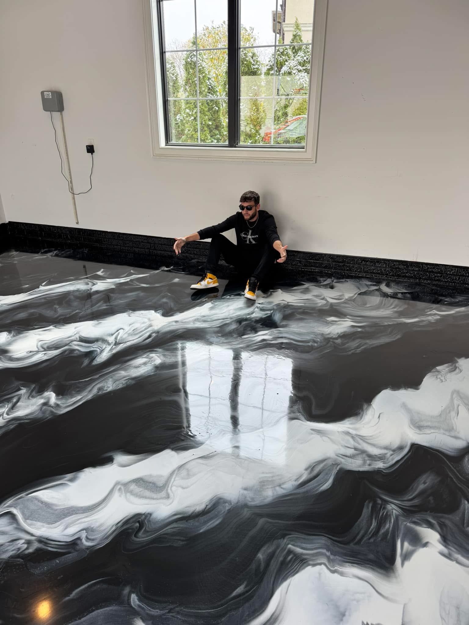 Person sitting on a glossy black-and-white marbled floor in a bright room near a window.