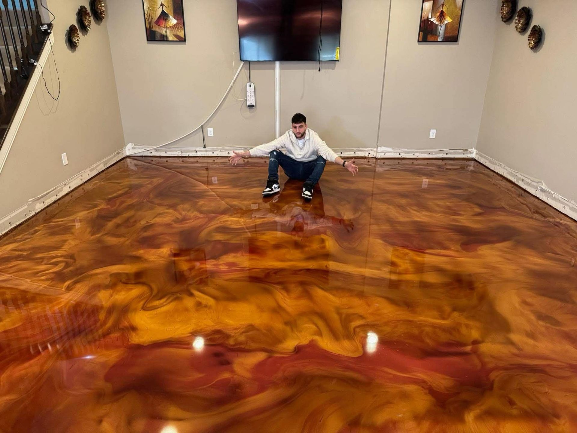 Person crouching on a glossy marbled floor in a large empty room with wall-mounted TV and speakers.