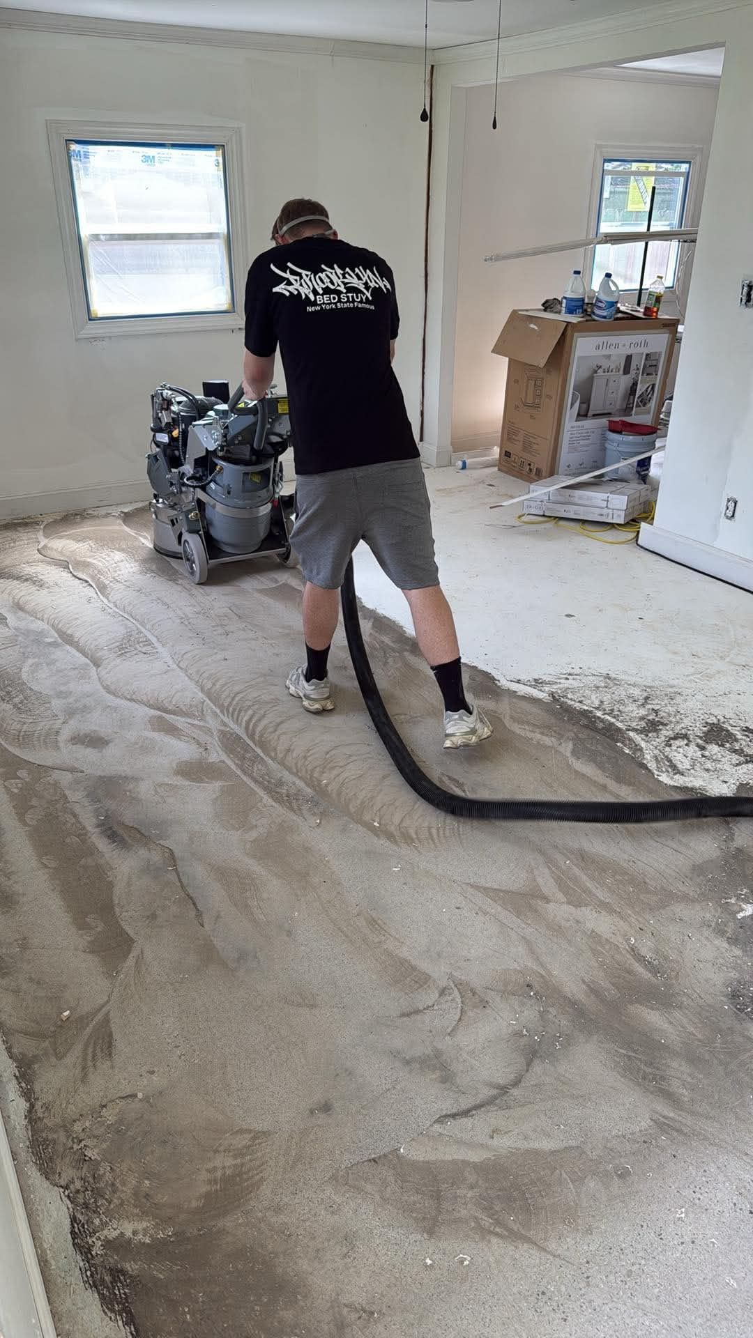 Worker sanding a dusty floor in an empty room with a floor sander and vacuum hose