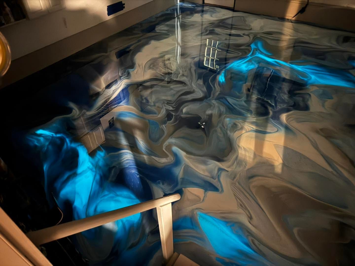 Abstract blue and silver swirls on a glossy floor with a wooden railing in the foreground