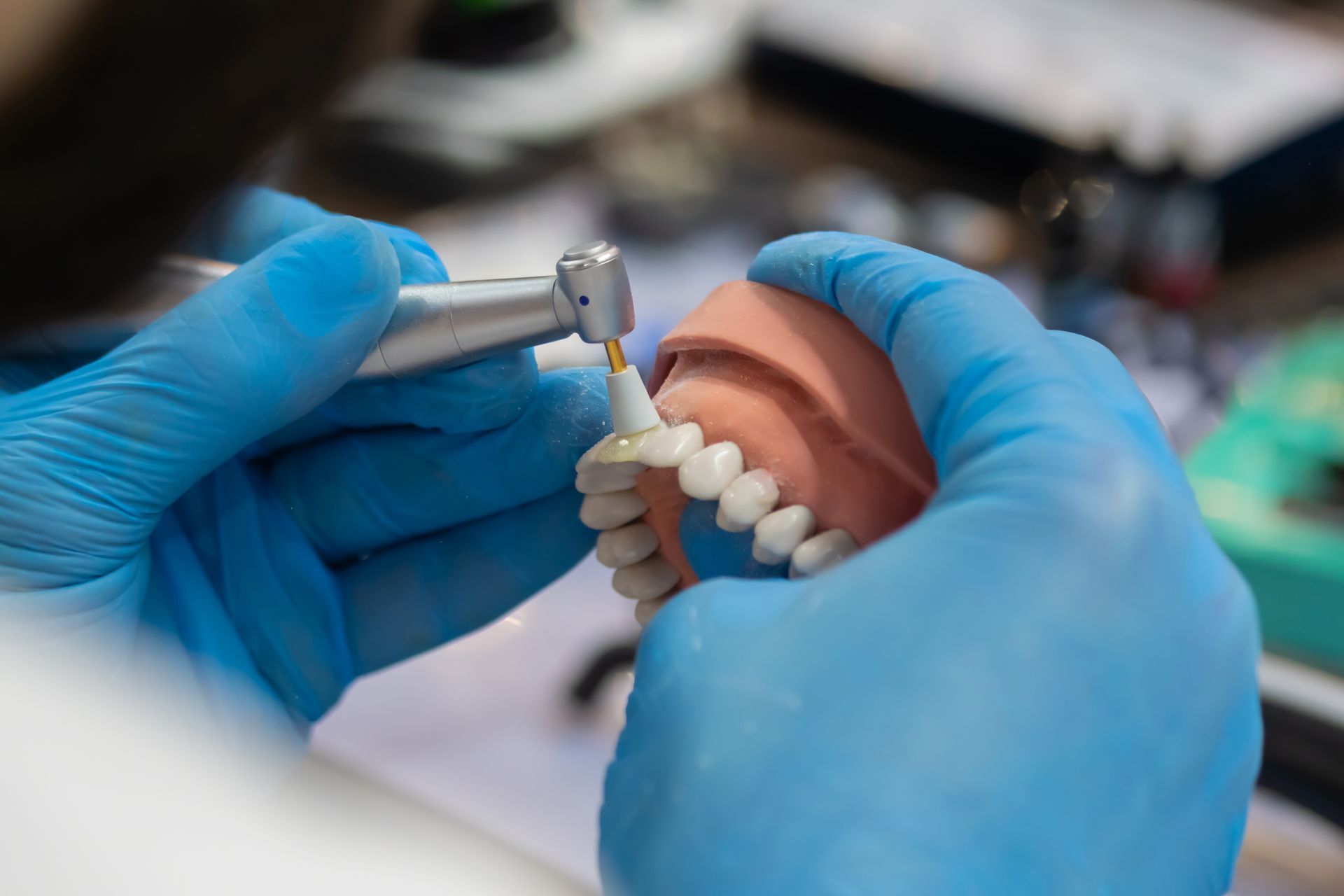 Hands in blue gloves holding dental tool, working on a model set of teeth.