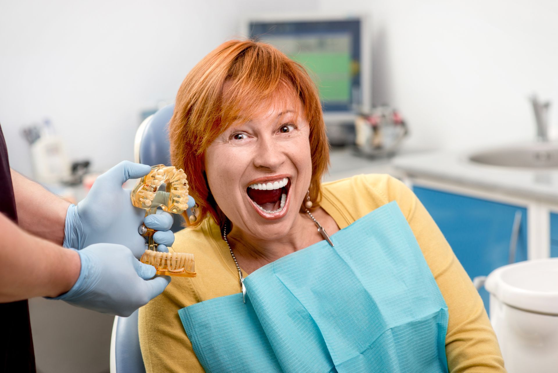 A senior woman smiling wide at a dental office with a dental technician holding dentures. A senior woman smiling wide at a dental office with a dental technician holding dentures.