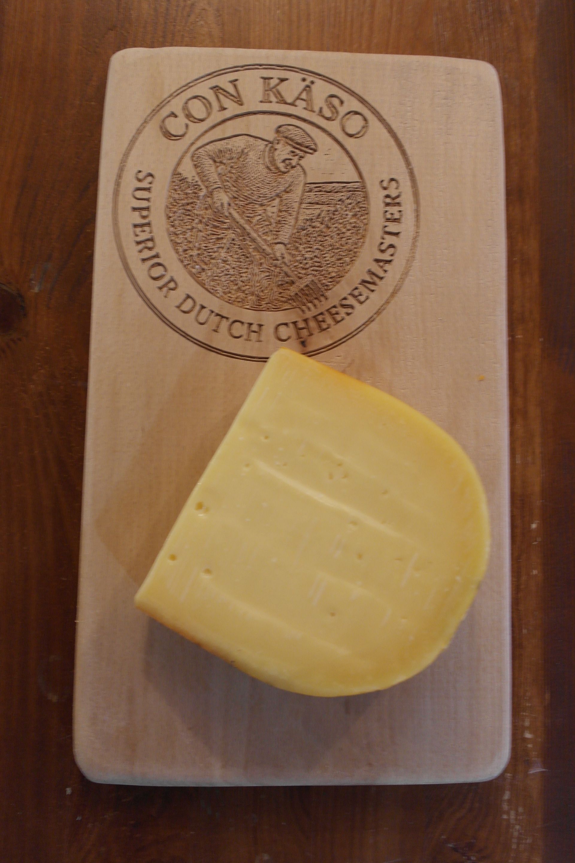 Ein Laib holländischer Käse, „De Gelaer“, mit einem angeschnittenen Stück. Gelbe Wachsrinde, blaues Etikett.
