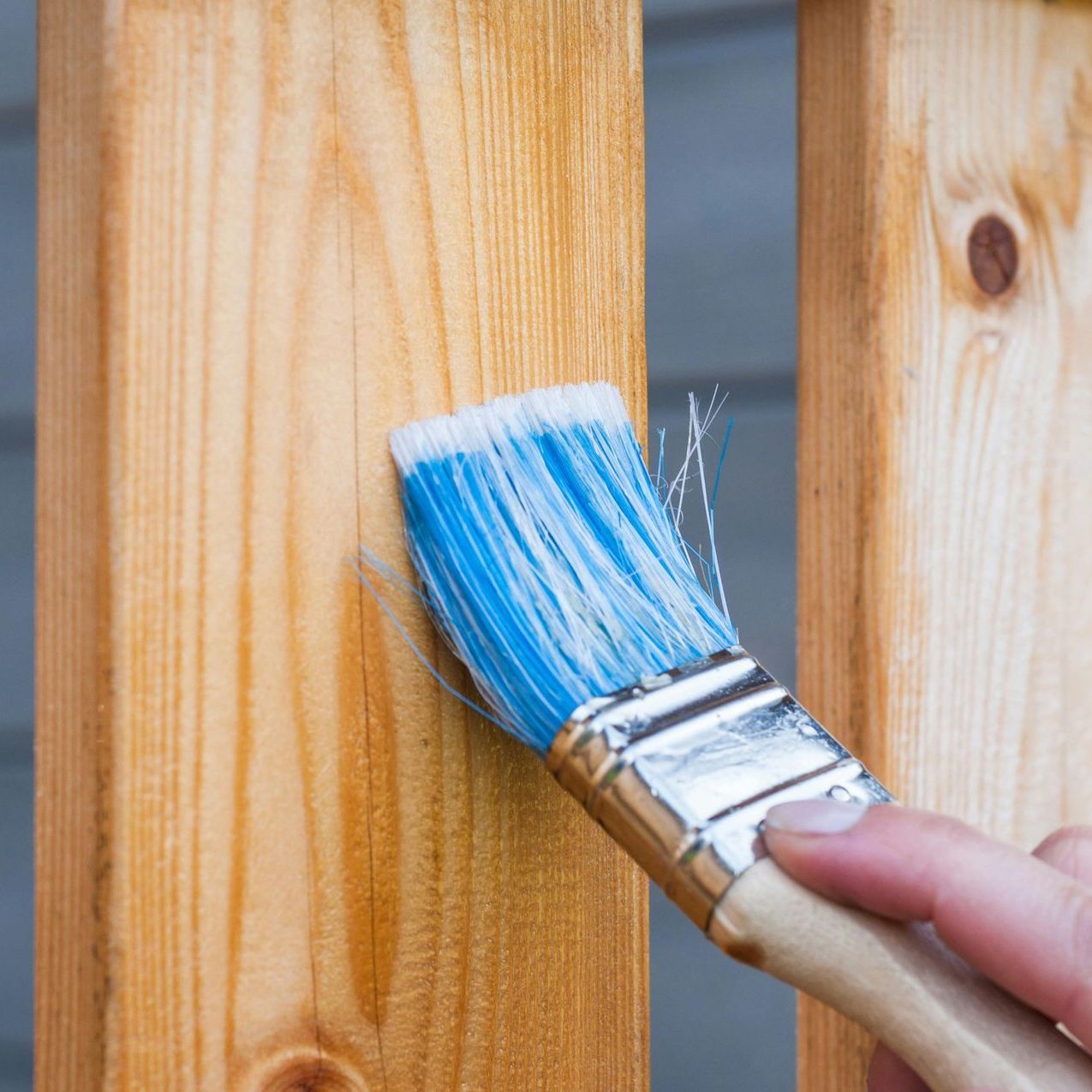 A person is painting a wooden post with a blue brush.