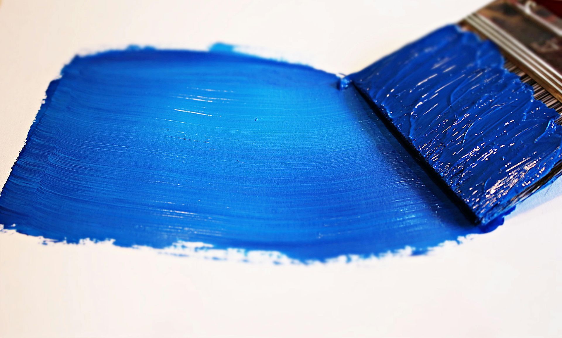 A paint brush with a stroke of blue paint on a white surface.