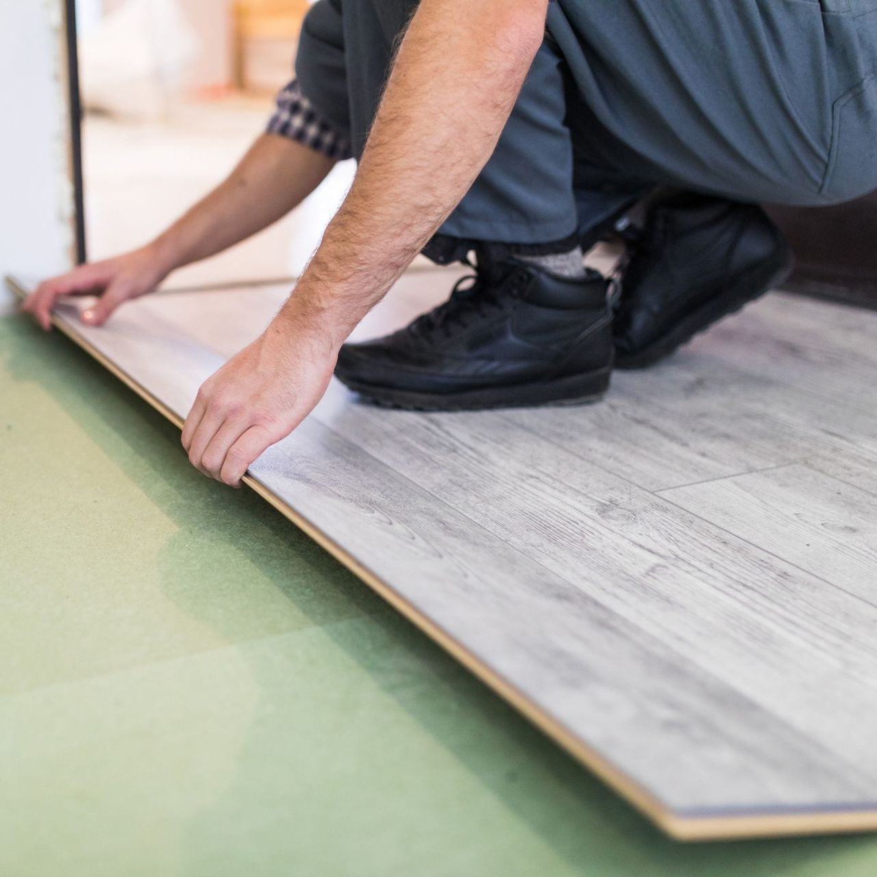 A man is kneeling down to install a wooden floor.