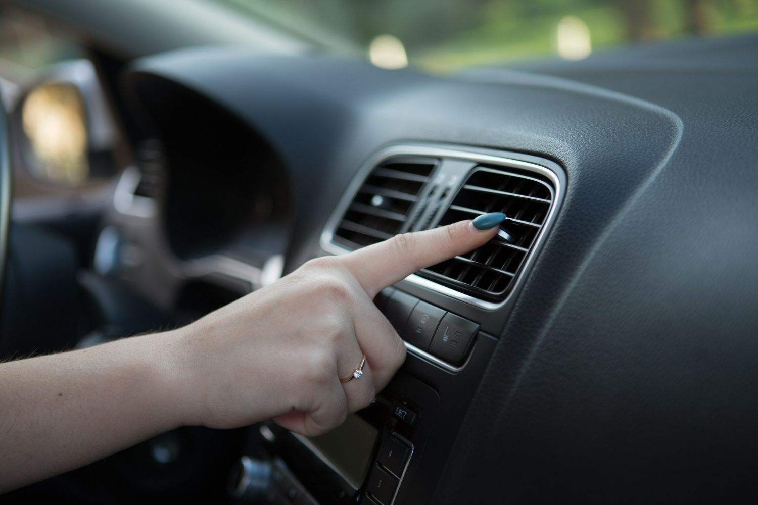 Hand touching a car dashboard air vent and control panel inside a vehicle