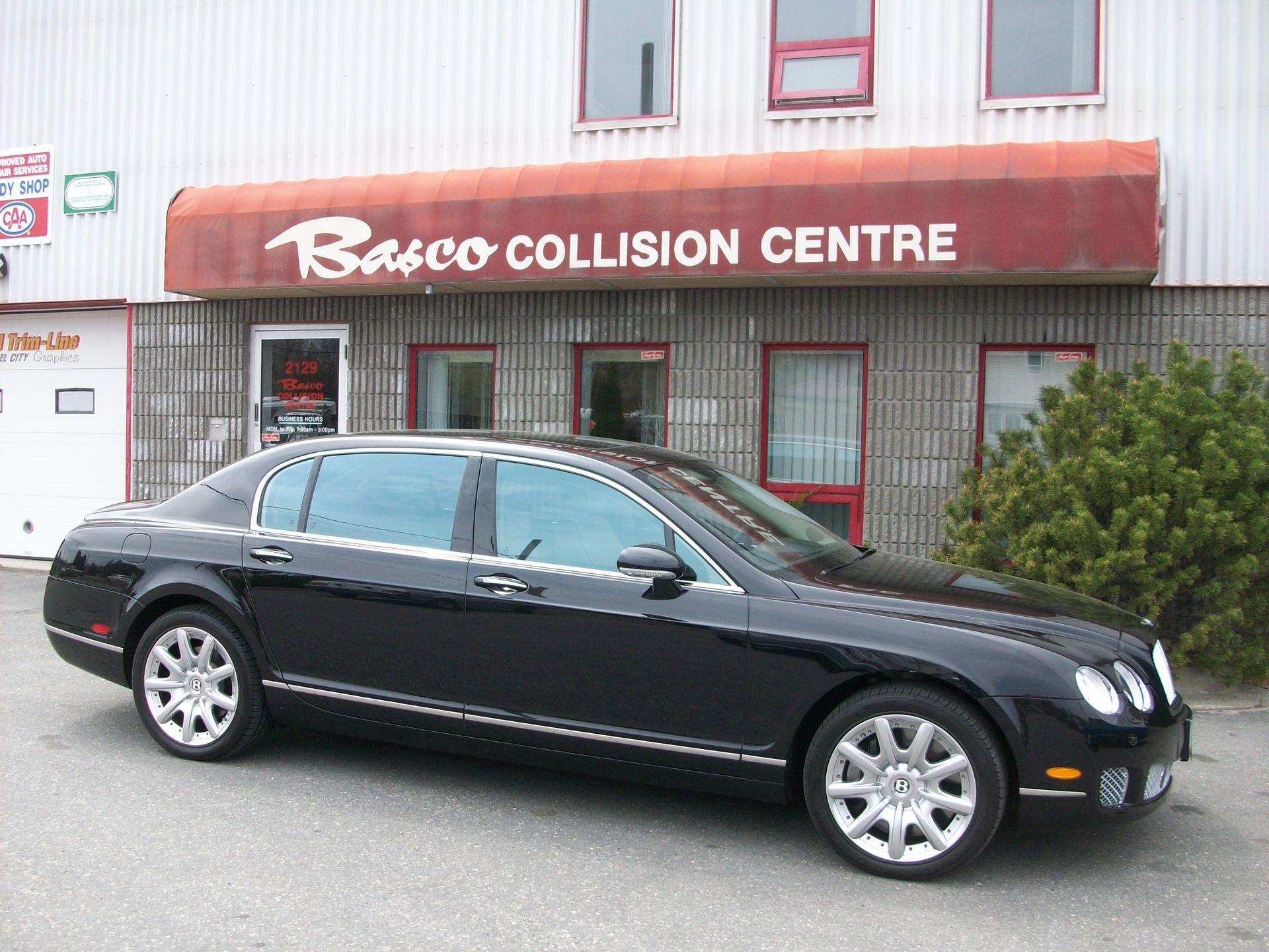 A black car is parked in front of a building that says barco collision centre
