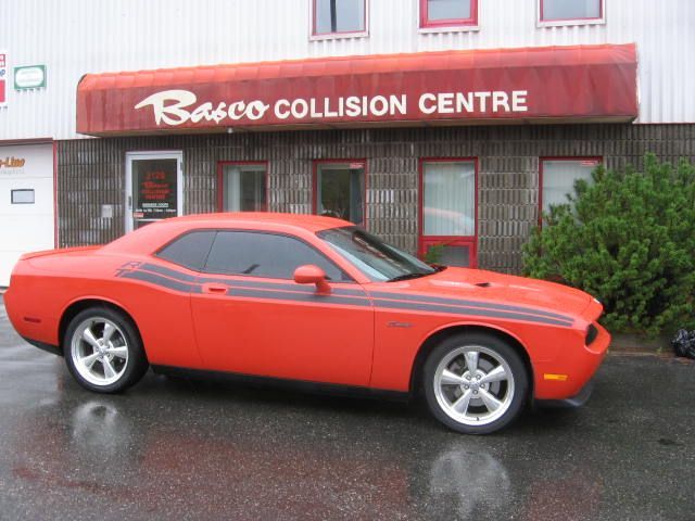 An orange car is parked in front of a building that says basco collision centre