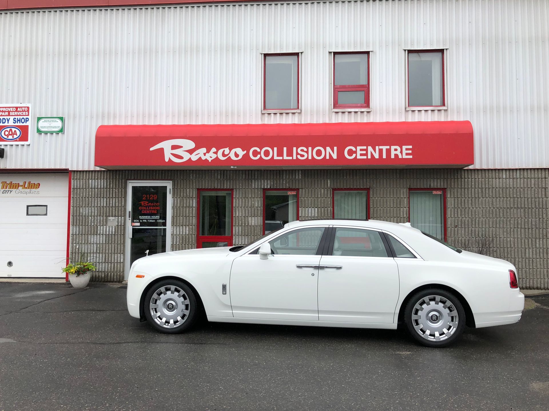 A white car is parked in front of a building that says barco collision centre