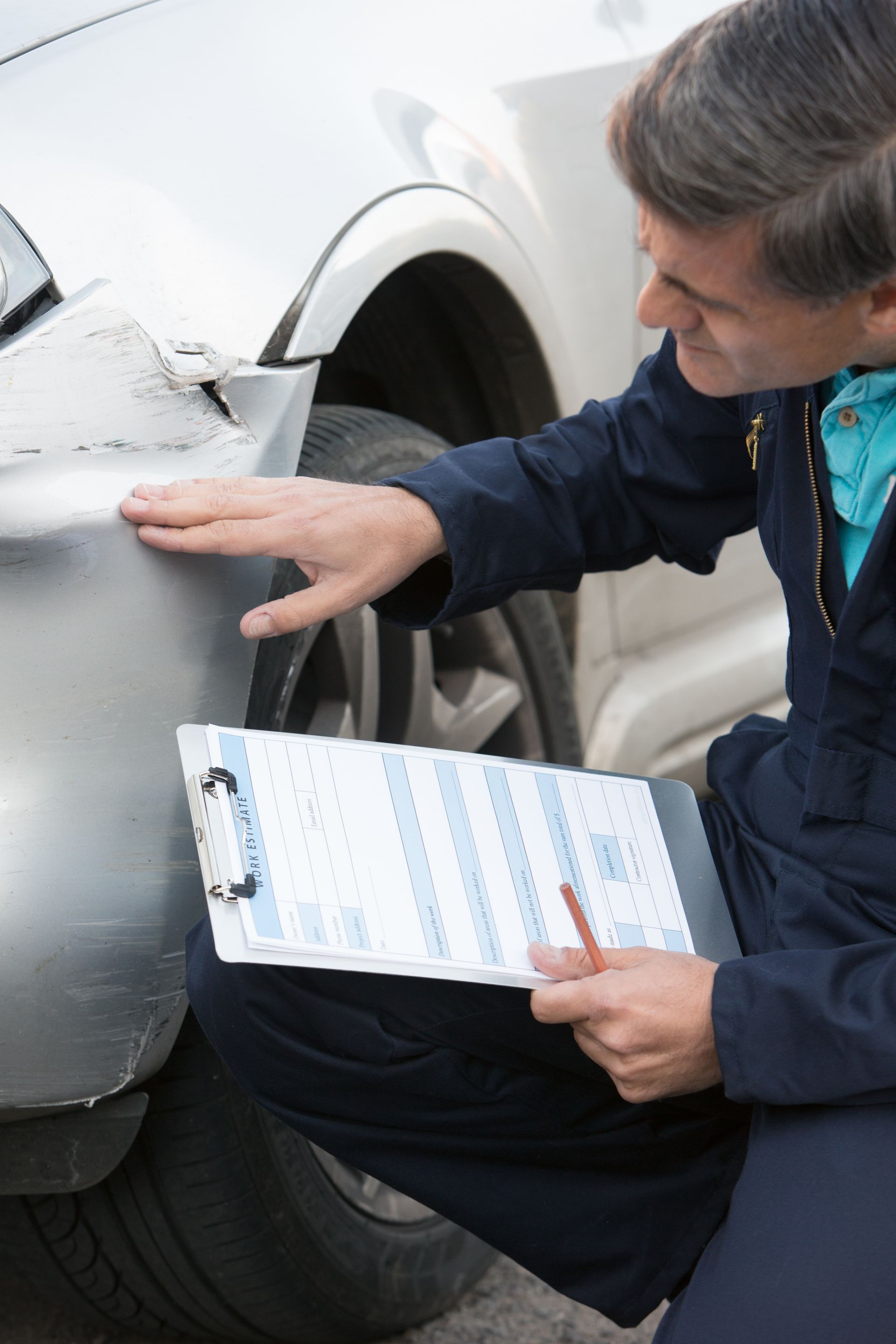 A man is writing on a clipboard next to a car