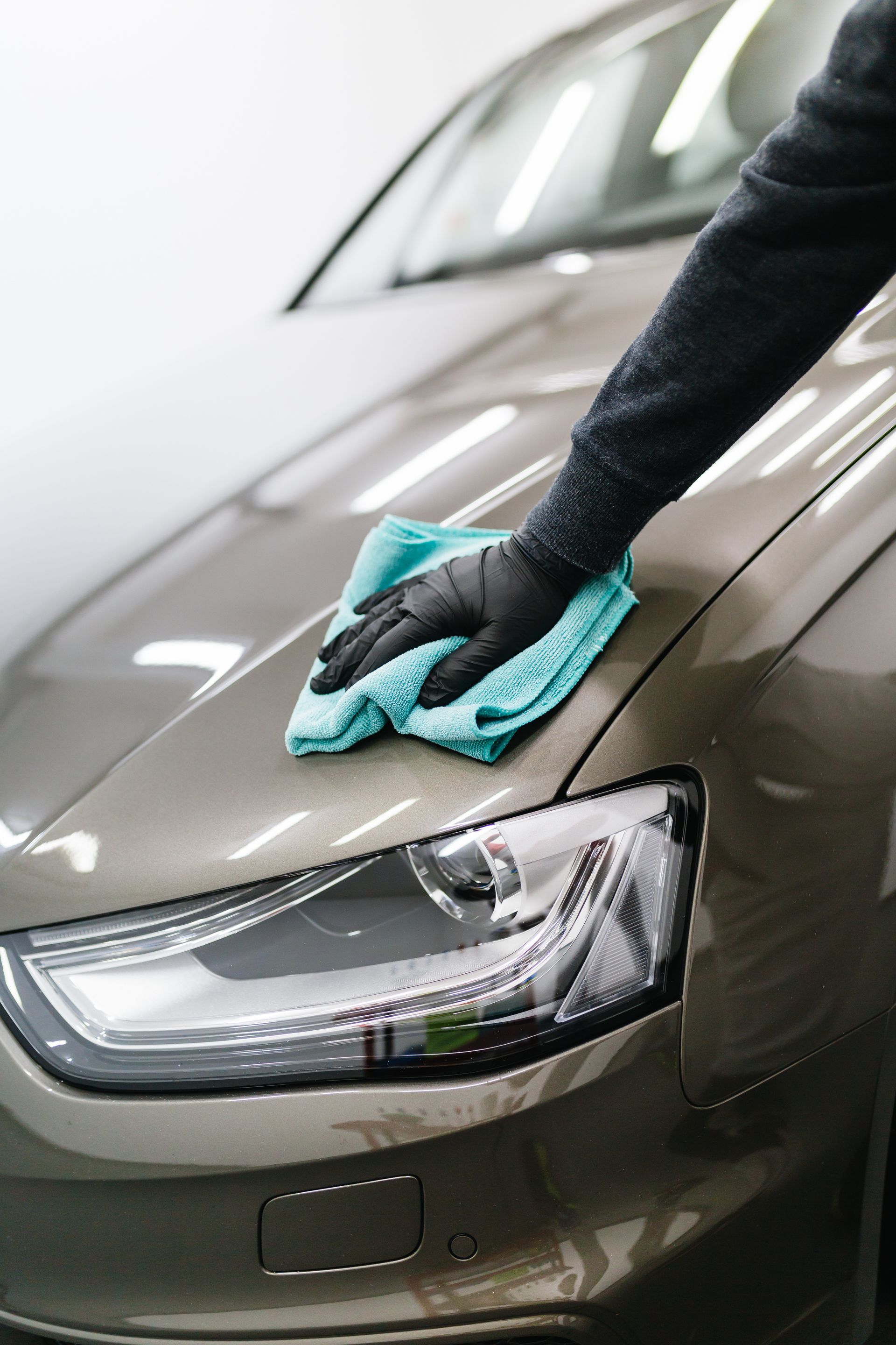 A person is cleaning a car with a towel and gloves.