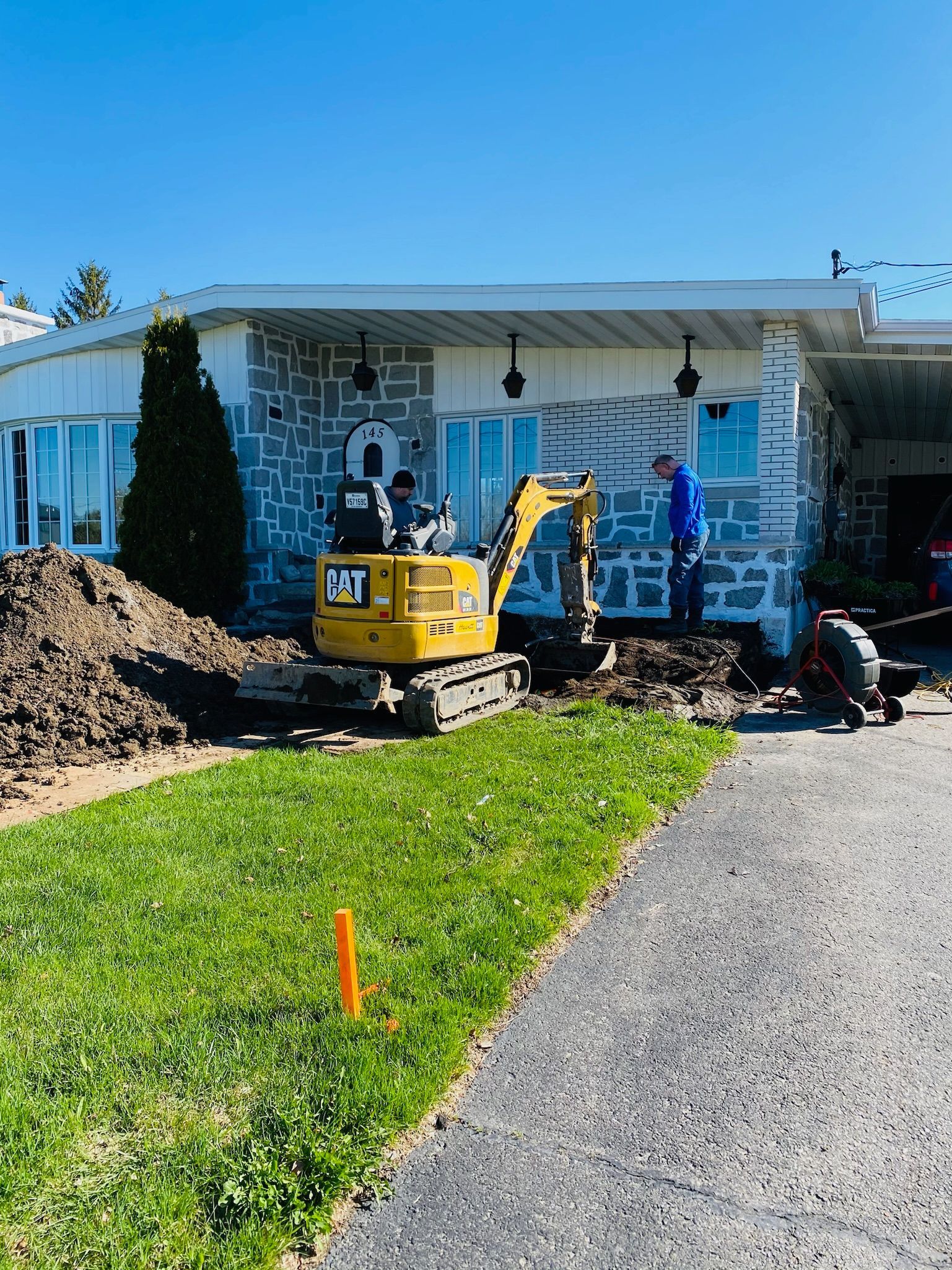Une excavatrice jaune est assise devant une maison.