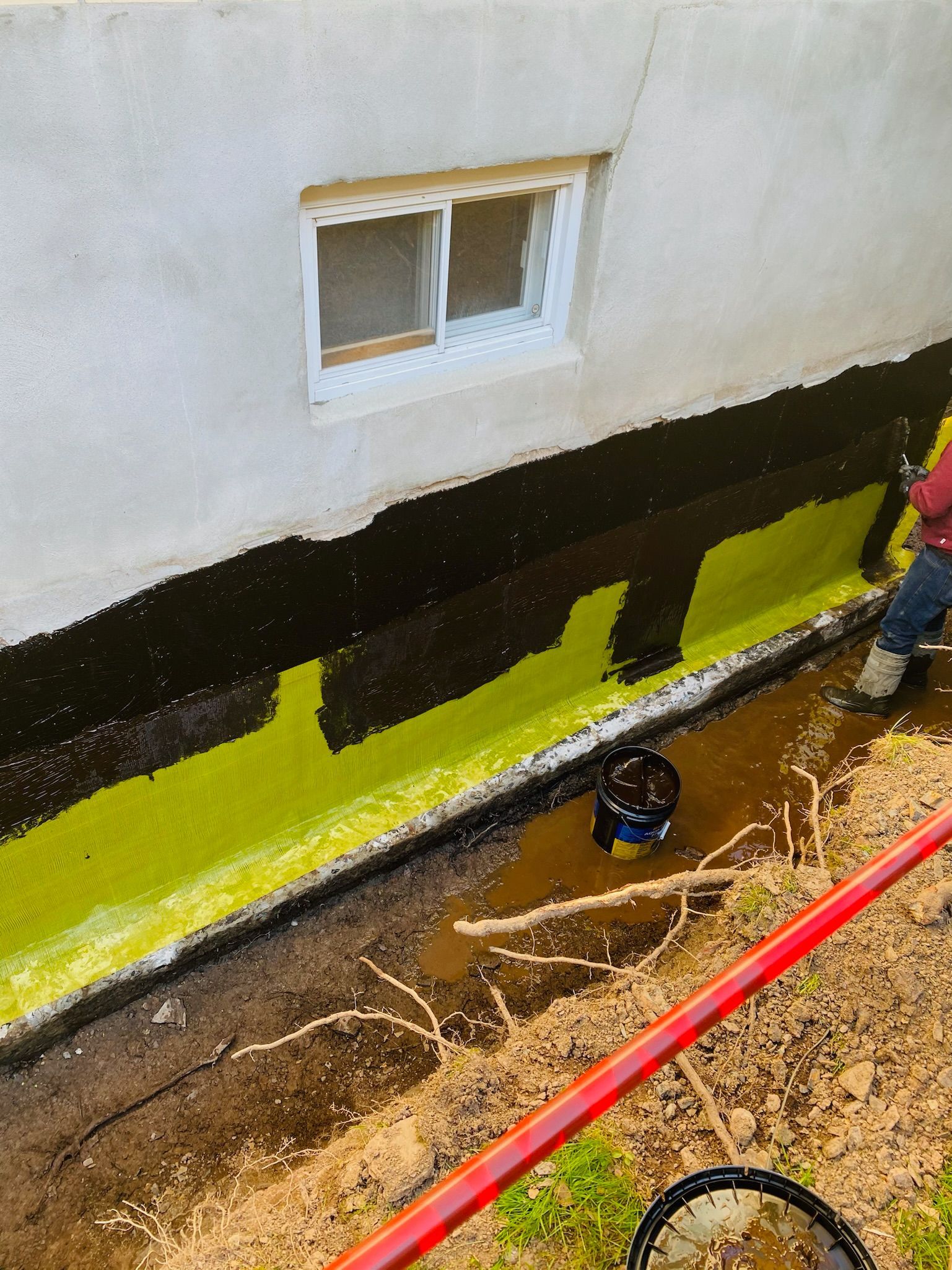 Un homme peint le côté d'une maison avec de la peinture jaune.