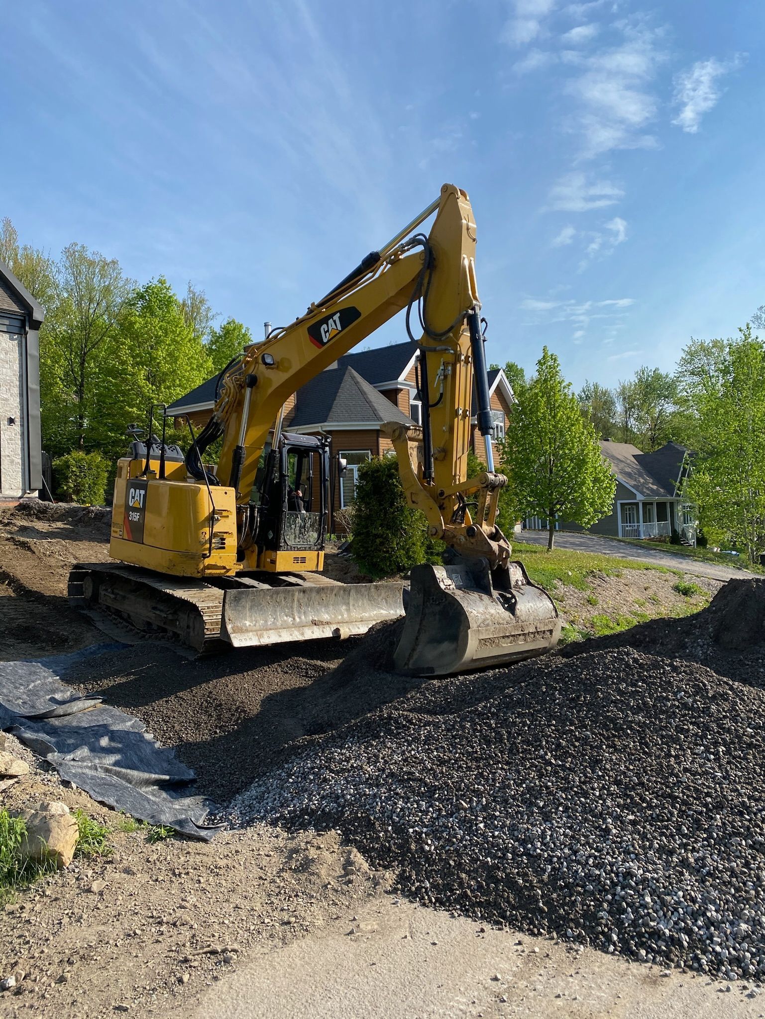 Une excavatrice jaune déplace de la terre devant une maison.