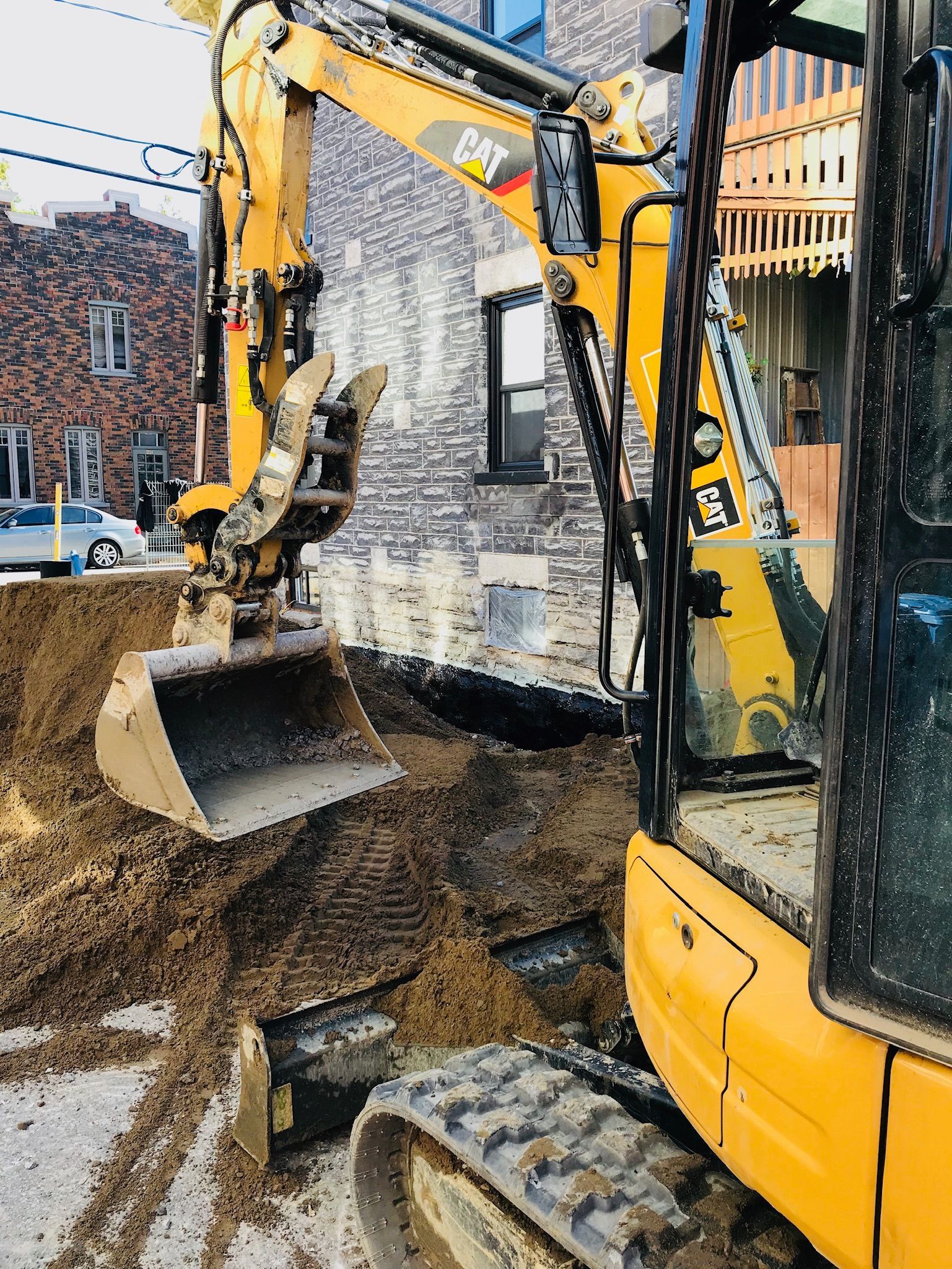 Une excavatrice jaune creuse un trou devant un bâtiment.