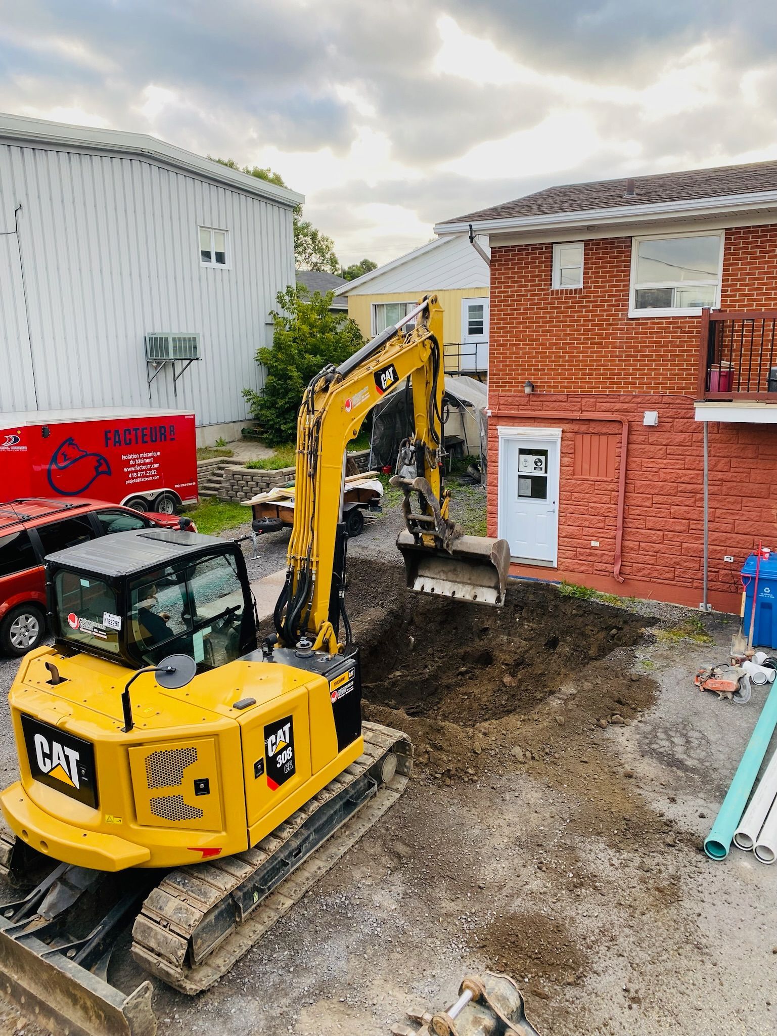 Une excavatrice jaune creuse un trou devant une maison en briques.