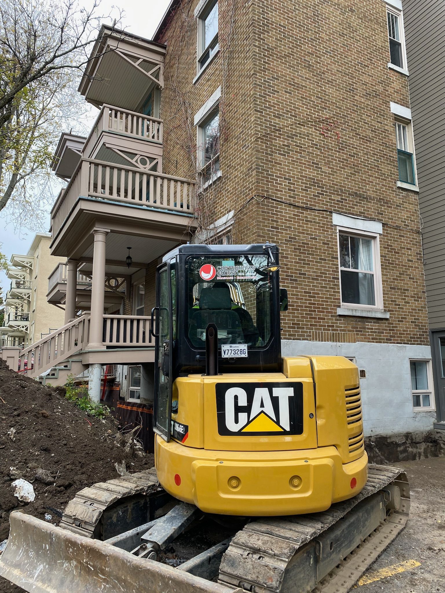 Une excavatrice jaune est garée devant un bâtiment en briques.