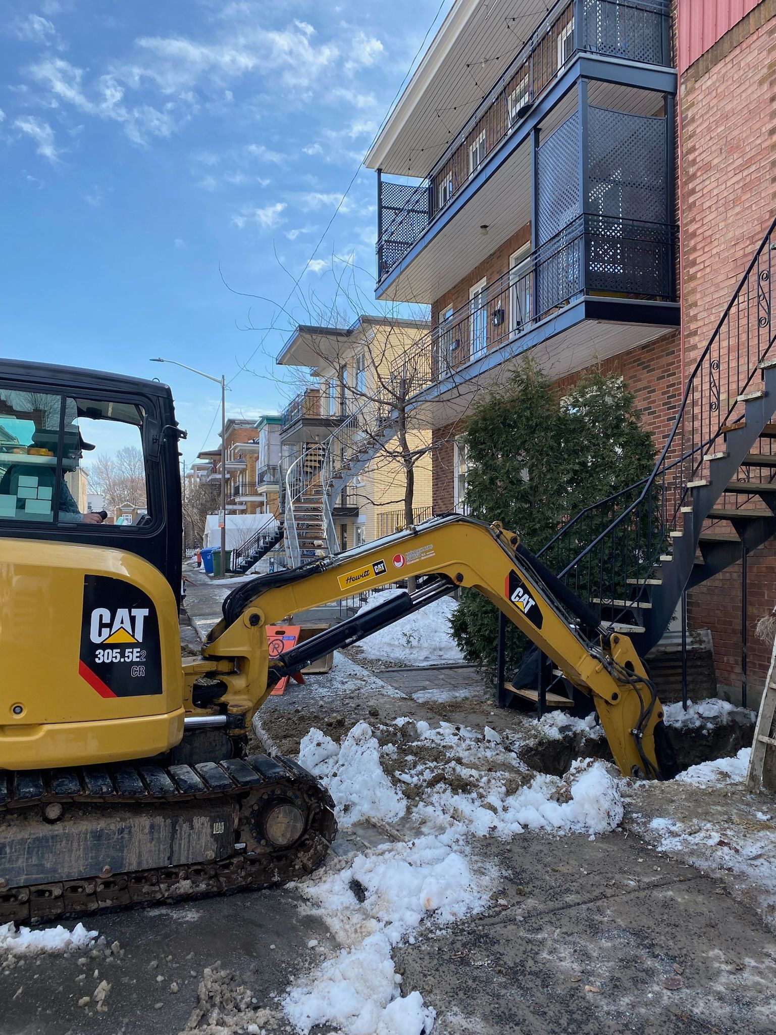 Une excavatrice à chat creuse un trou dans la neige devant un bâtiment.