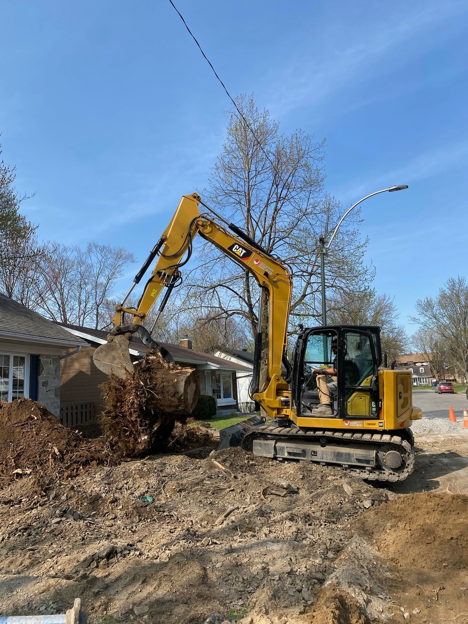 Une excavatrice jaune creuse un trou devant une maison.