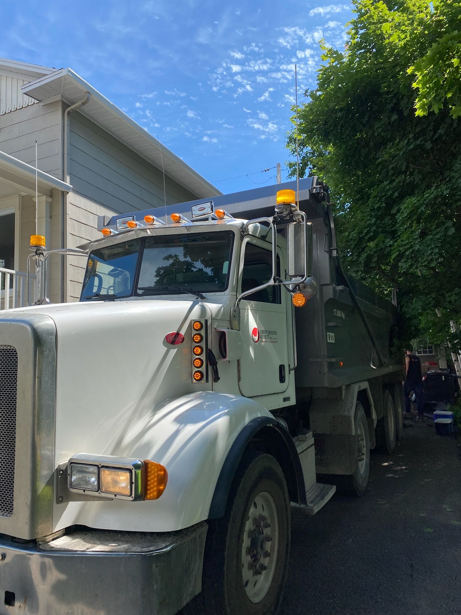 Un camion à benne basculante blanc est garé devant une maison