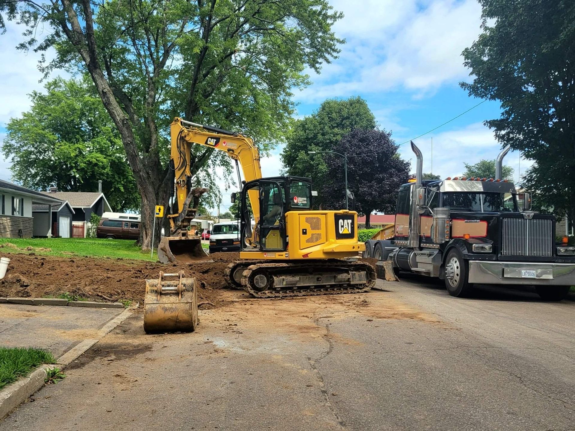 Une excavatrice jaune est assise sur le bord de la route à côté d'un semi-remorque.