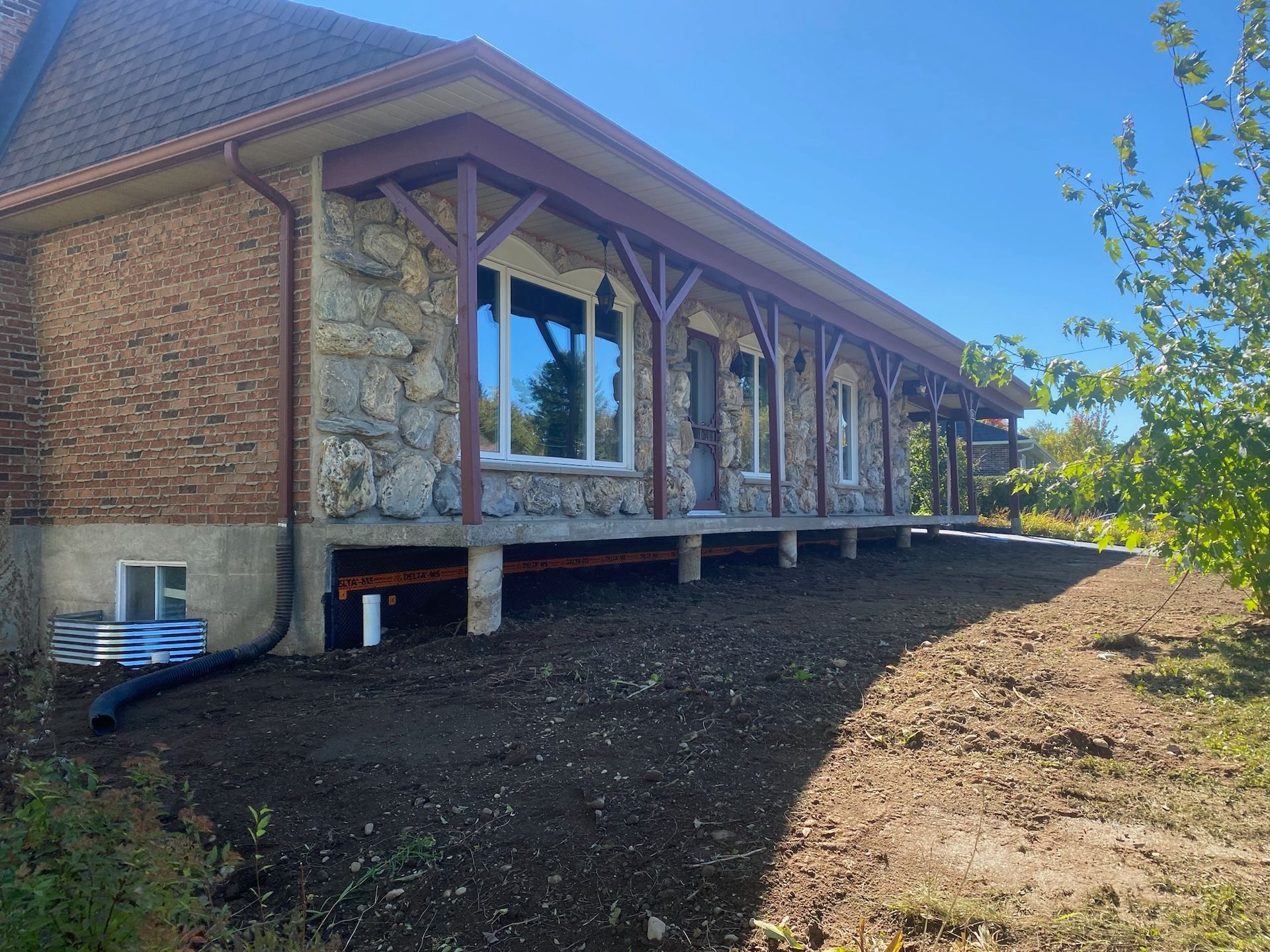 Une grande maison en briques avec un porche est située au sommet d'une colline de terre.