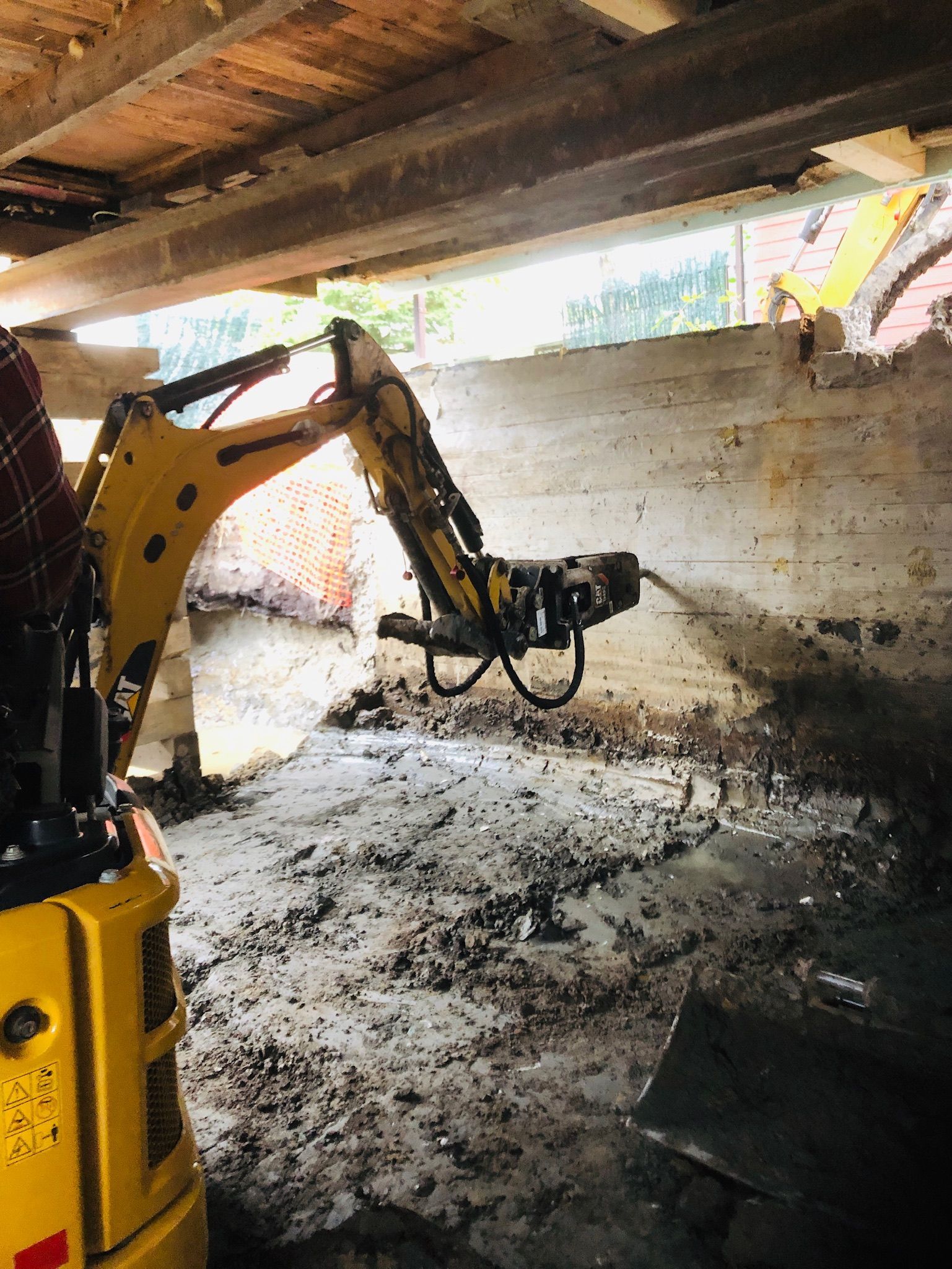 Une excavatrice jaune travaille sous une maison.