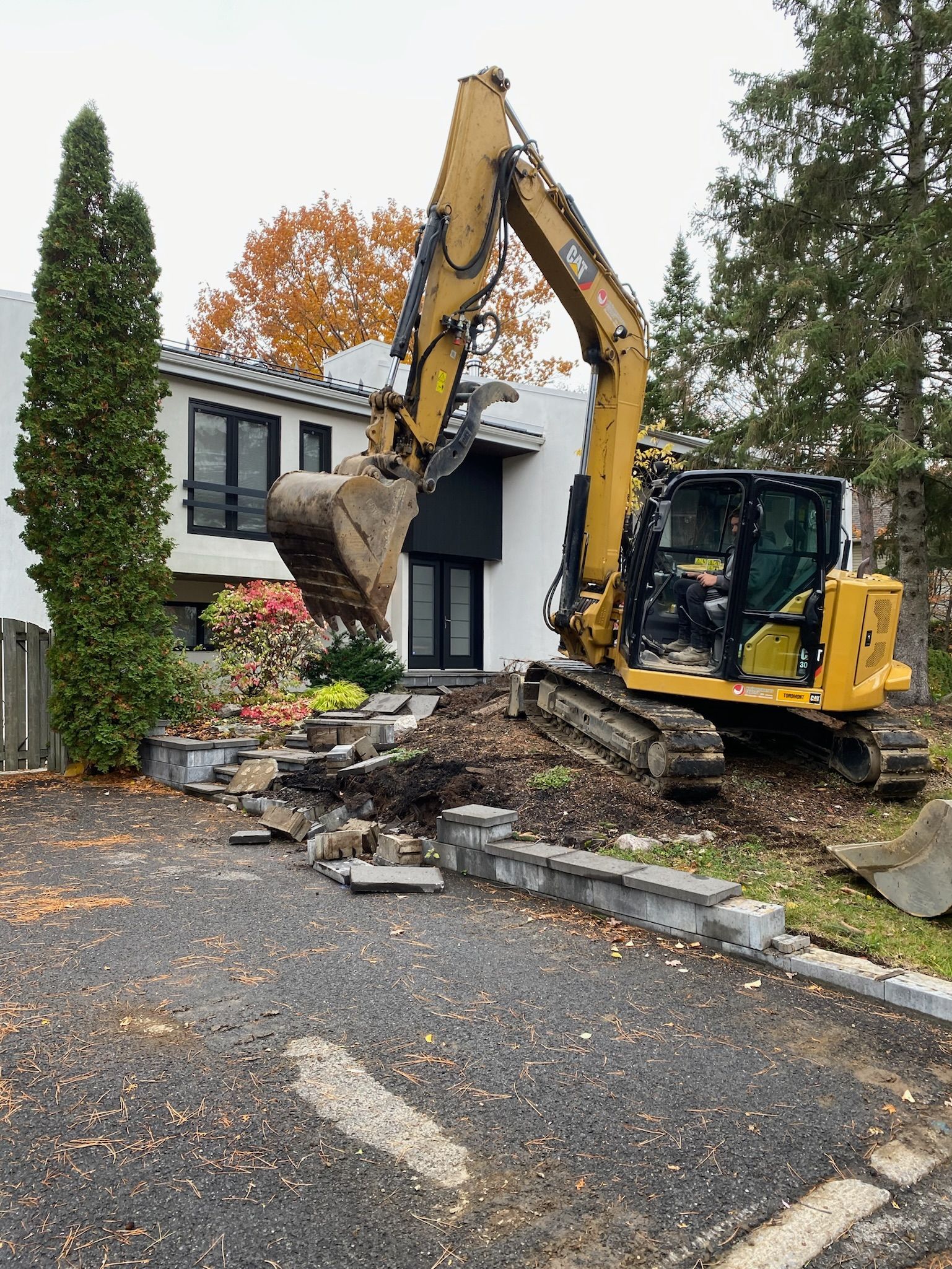 Une excavatrice jaune creuse un trou devant une maison.