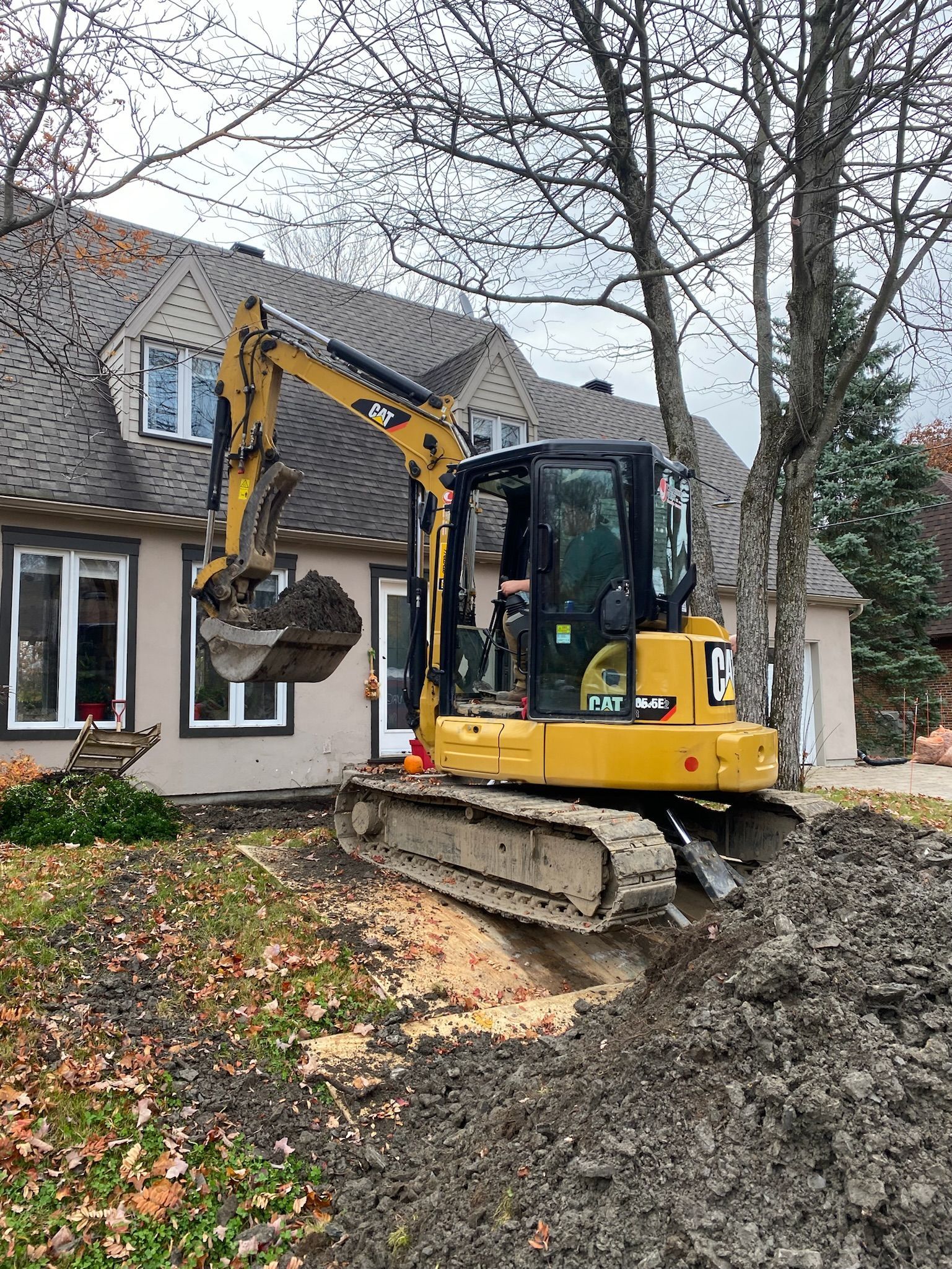 Une excavatrice jaune creuse un trou devant une maison.