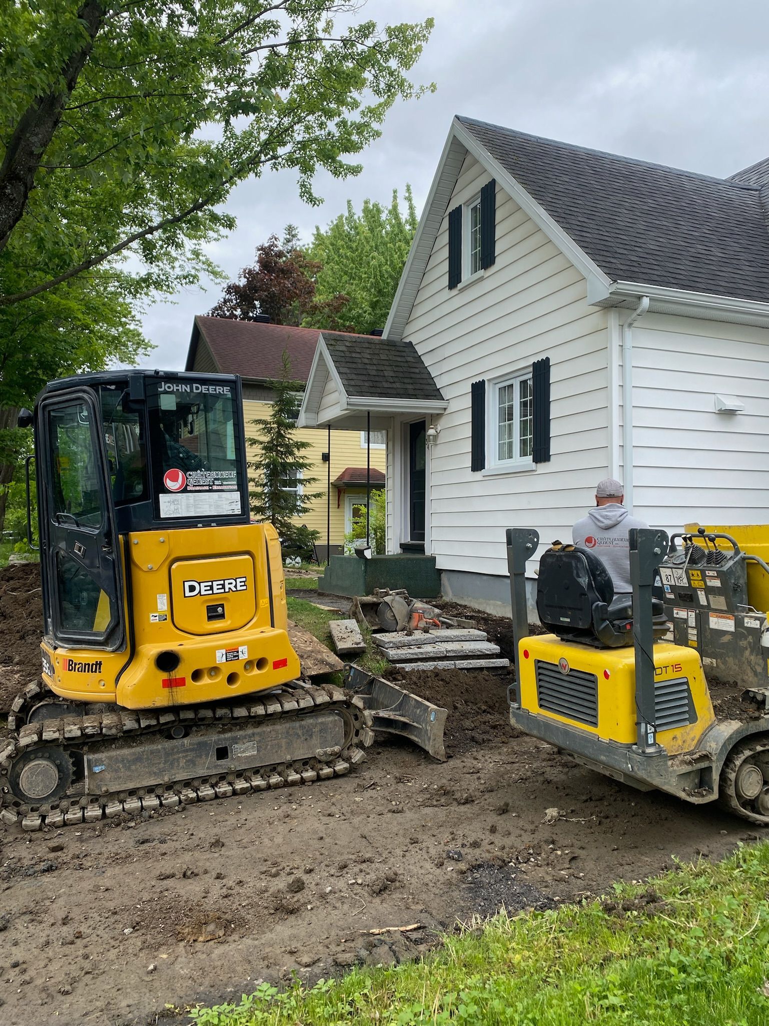 Un bulldozer jaune est garé devant une maison blanche.