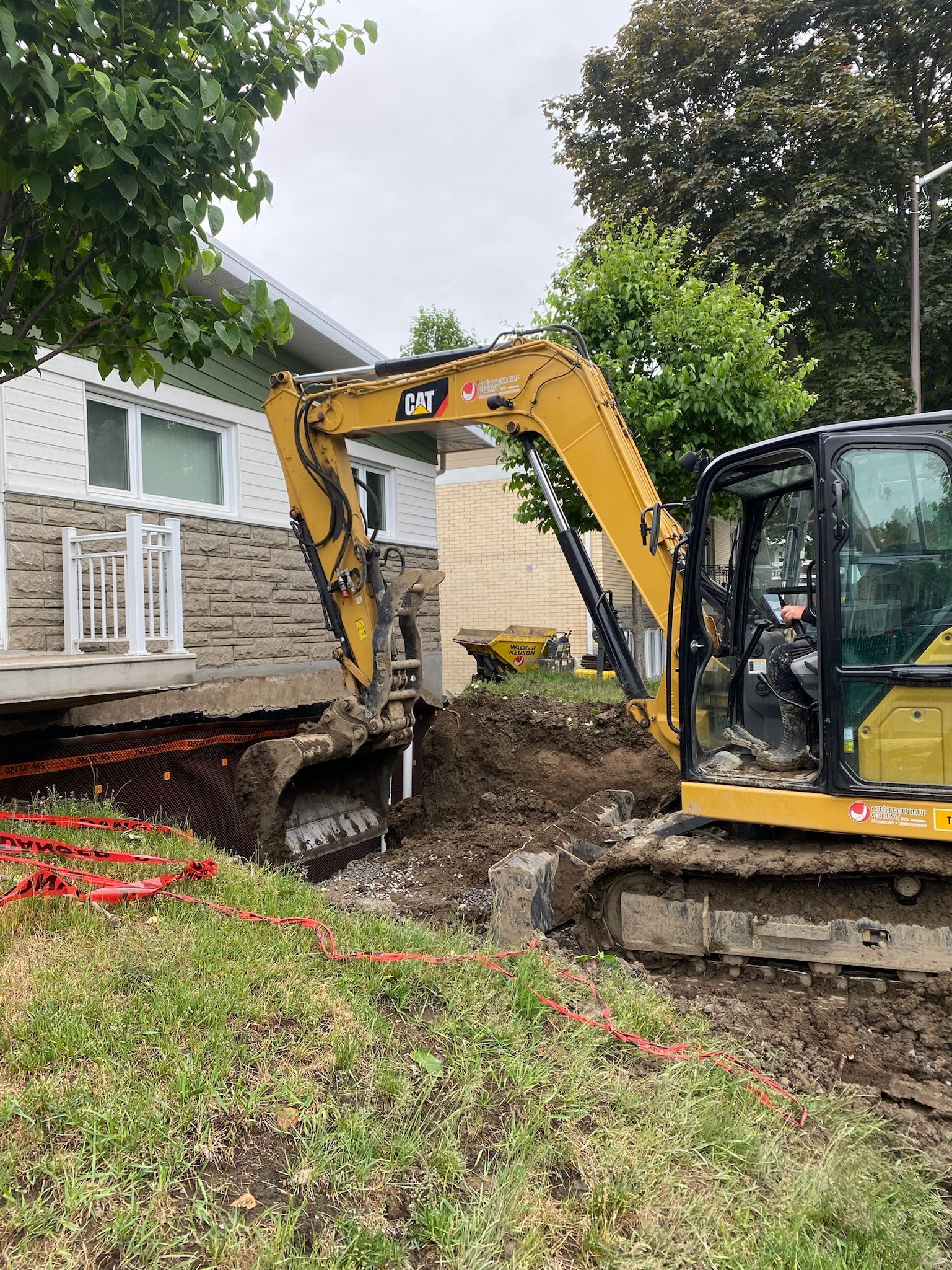 Une excavatrice jaune creuse un trou devant une maison.