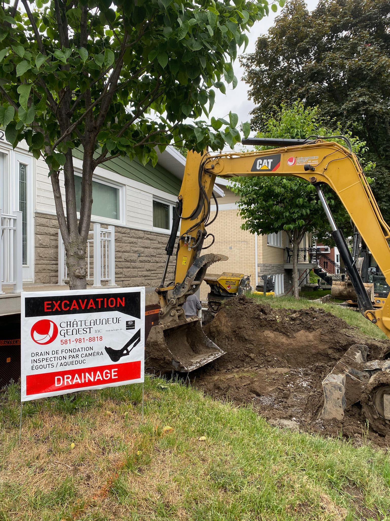 Une excavatrice creuse un trou devant une maison.