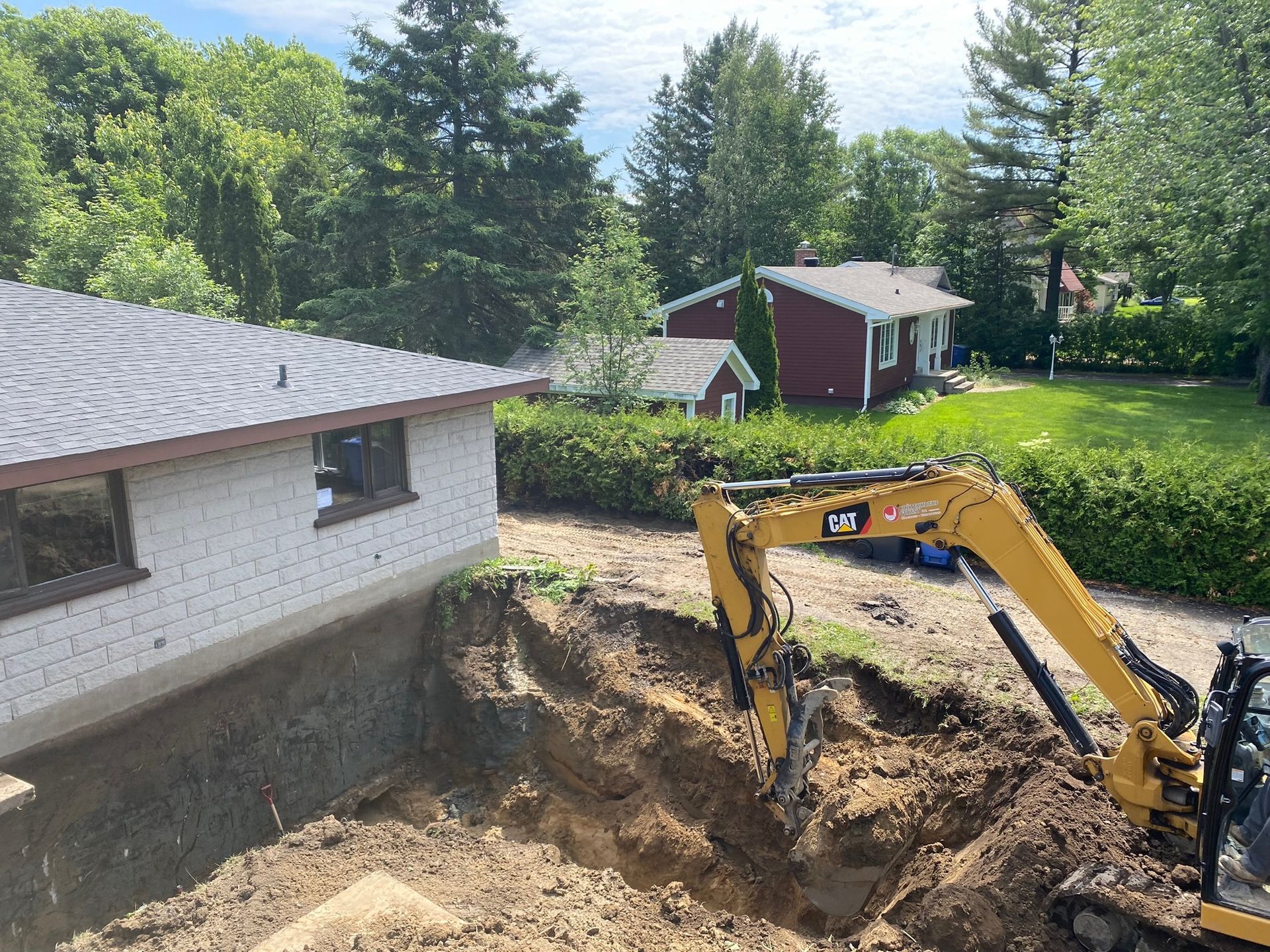 Une excavatrice jaune creuse un trou devant une maison.