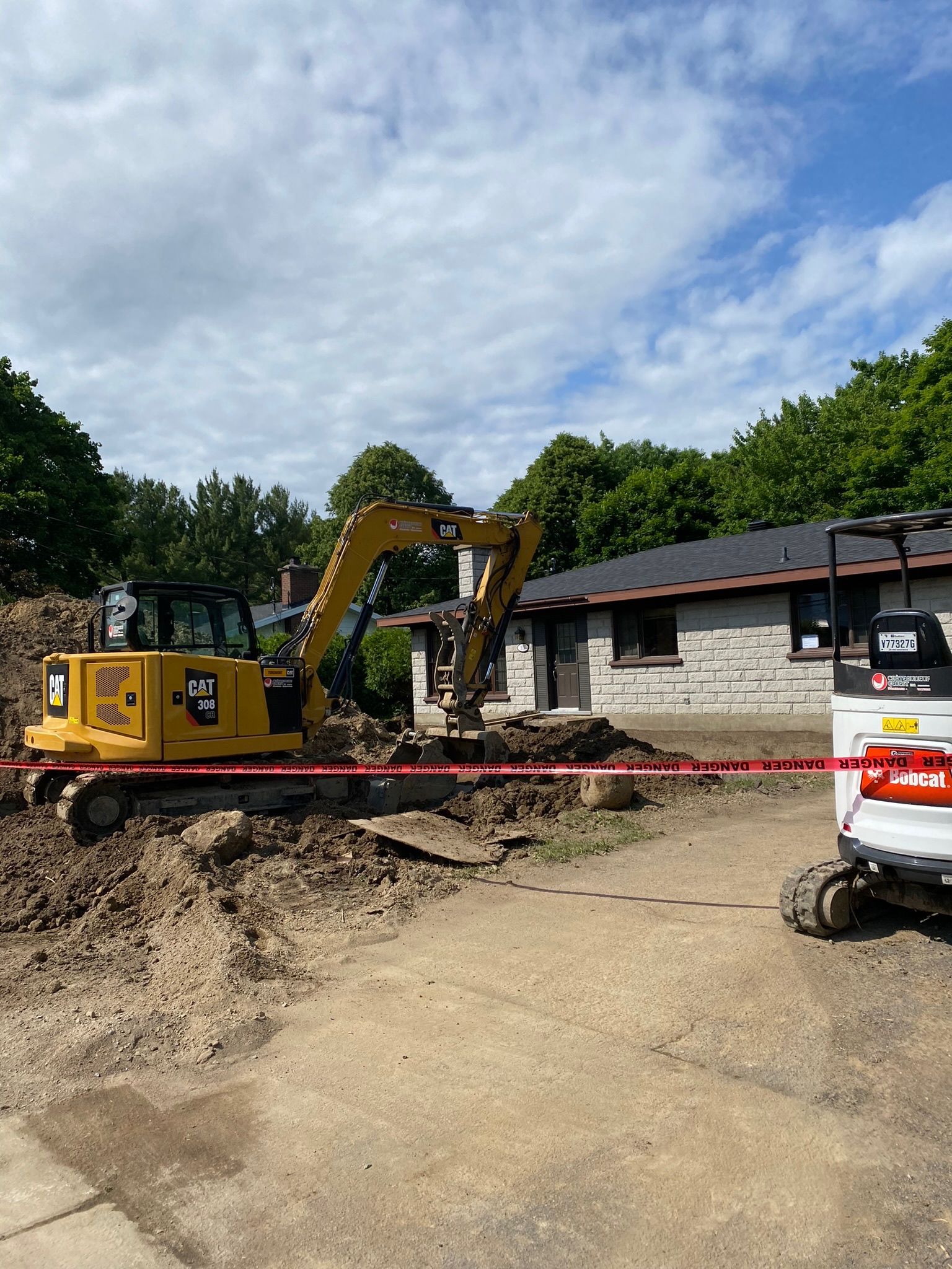Une excavatrice jaune travaille sur un chantier devant une maison.