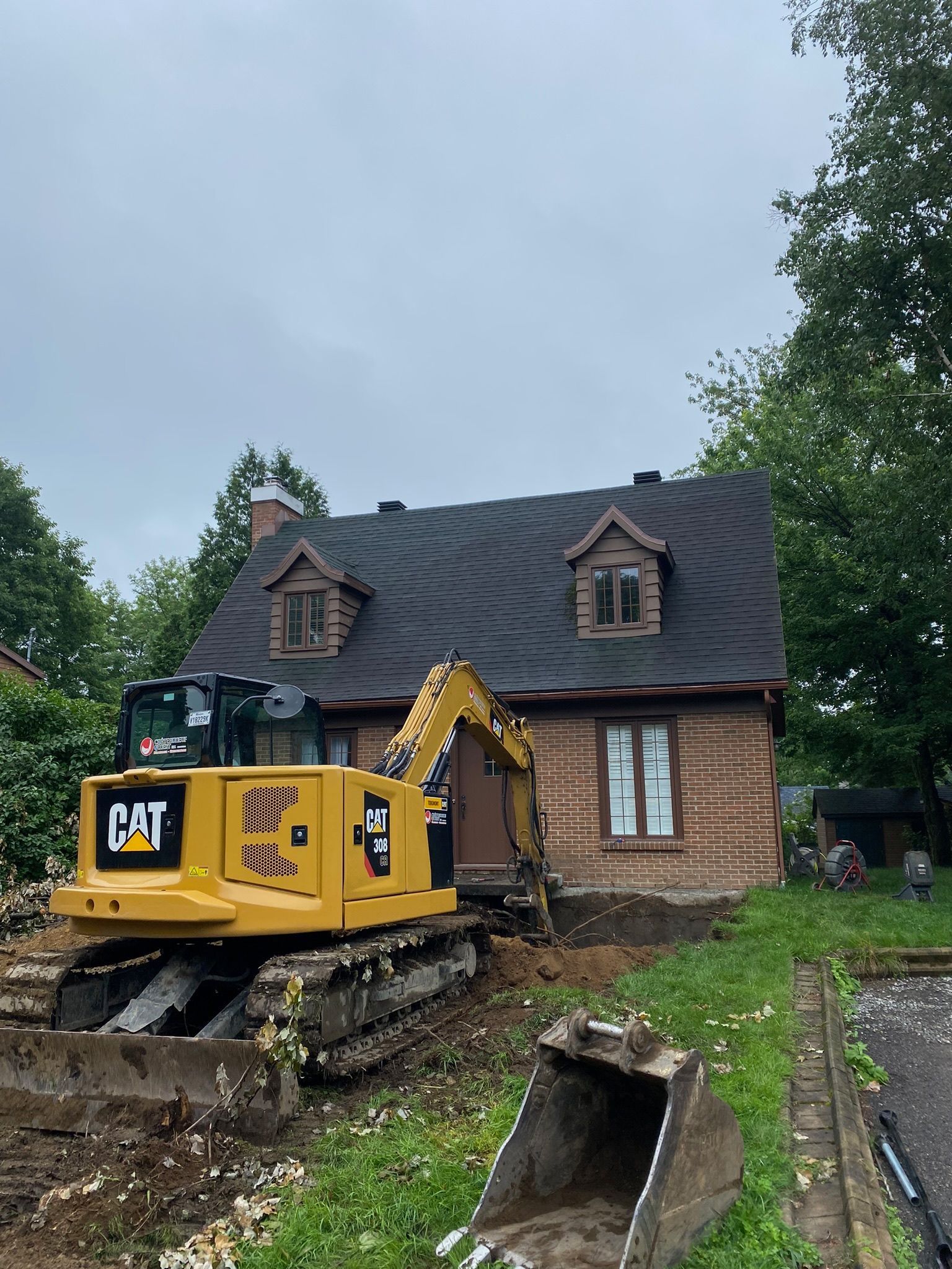 Une excavatrice jaune est garée devant une maison en briques.