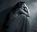 Donna accovacciata nell'ombra, con il viso tra le mani, che indossa un abito svolazzante.