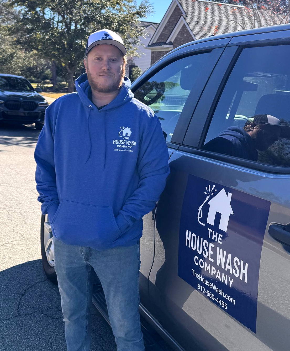 Owner Robbie Coggins in blue hoodie and hat stands beside a car with 